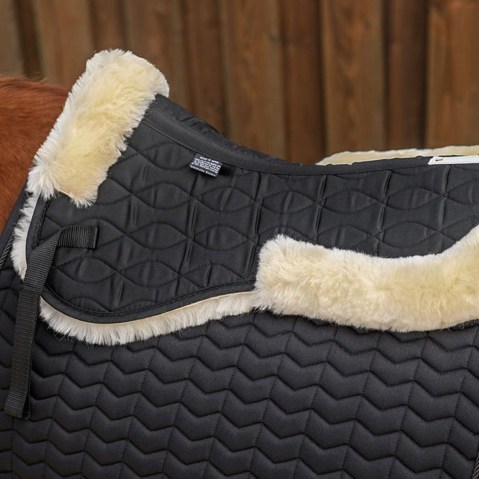 Black quilted saddle pad with beige fleece lining on a horse.