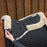 Black quilted saddle pad with beige fleece lining on a horse, against a wooden fence background.